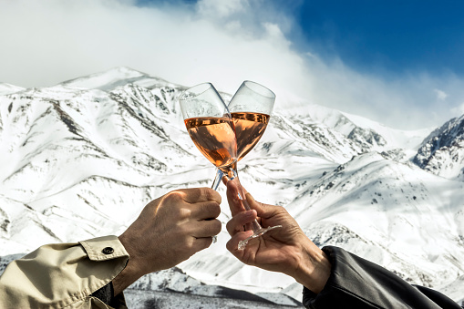 Couple toasting with rose champagne at the foot of the snowy mountains.
