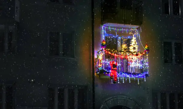 Photo of red jingle bells, lights, fir branches with ornaments on balcony in european city street