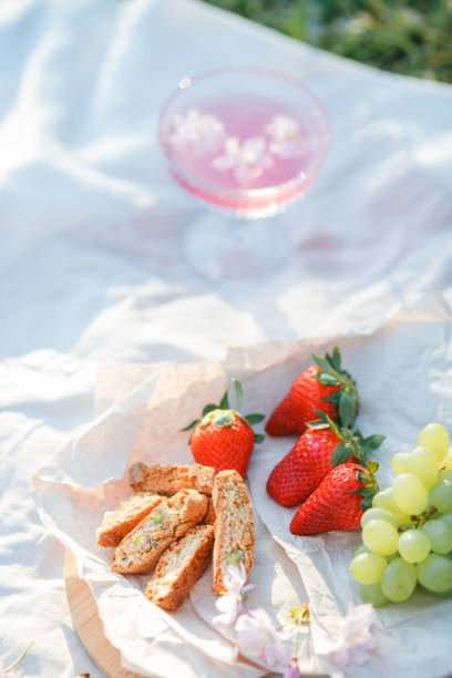 Spring picnic in nature. A glass of pink champagne with sakura flowers, a wicker bag, a hat, Italian. Wine. Spring.