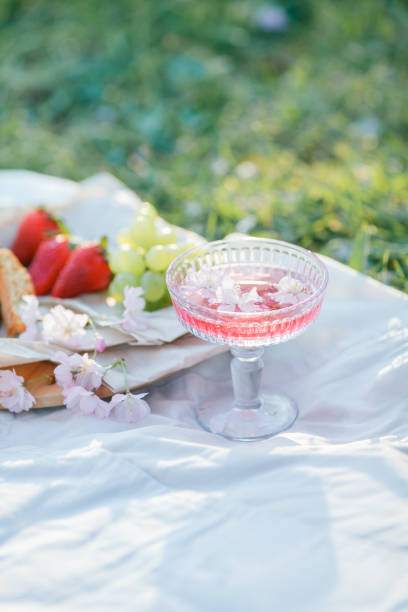 Spring picnic in nature. A glass of pink champagne with sakura flowers, a wicker bag, a hat, Italian. Wine. Spring.