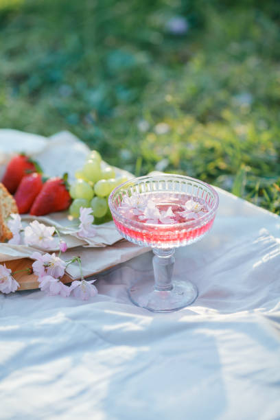 Spring picnic in nature. A glass of pink champagne with sakura flowers, a wicker bag, a hat, Italian. Wine. Spring.