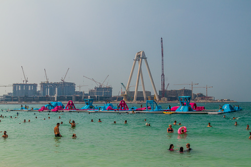DUBAI, UAE - OCTOBER 21, 2016: People bathing at Marina Beach in Dubai, United Arab Emirates. Ain Dubai ferris wheel construction site in the background.