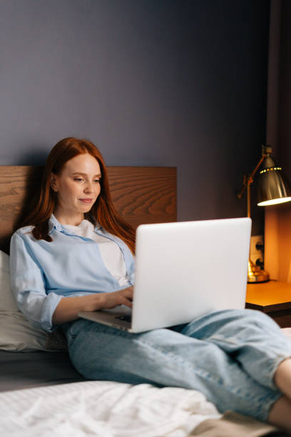 istock Cute redhead young woman lying on bed and using computer laptop for using social media. 1311344511