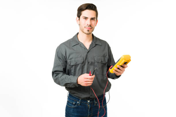 Portrait of a handsome male technician working Serious young man working as an electrician while holding a multimeter. Hispanic man technician making eye contact and using a work tool electrician multimeter stock pictures, royalty-free photos & images