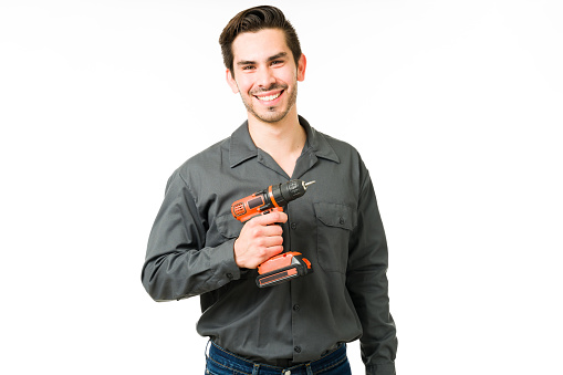 Portrait of an attractive young man holding an electric drill and working as a constructor. Smiling latin man and repairman feeling happy on his job