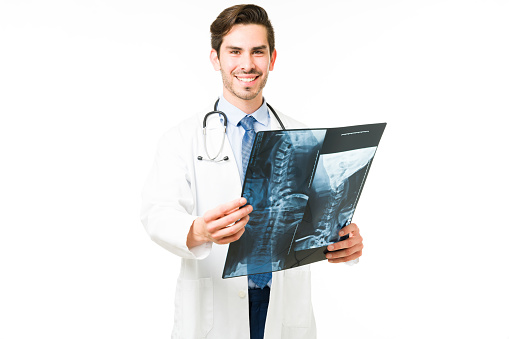 Orthopedist making eye contact and smiling while holding a bone scan of a patient in the hospital. Young doctor posing against a white background