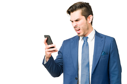 Upset professional man feeling angry and furious while looking at a text or email on a smartphone. Young businessman having a fight with a coworker or client on the phone