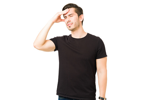 Worried young man having a bad headache or migraine. Stressed hispanic man rubbing his forehead and posing in a white background