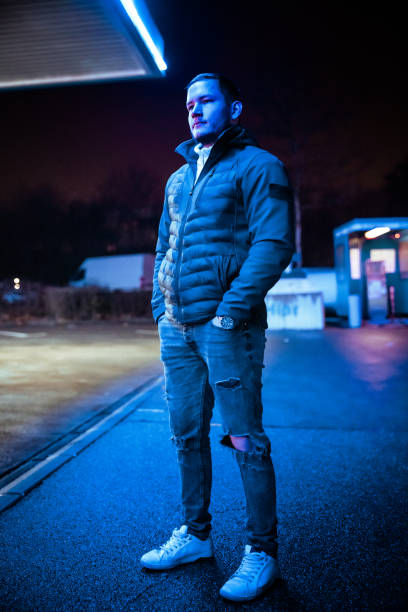 istock Young Man waiting at neon blue illuminated Gas Station at Night 1311349095