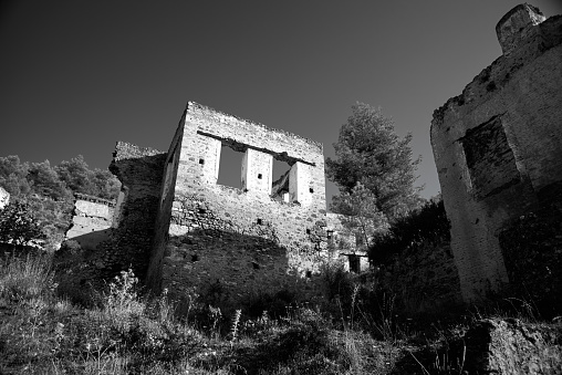 The old ruins on the hillside Greek ghost village of Kayakoy, formerly known as Lebessos or Livissi. Sunny day, green trees. 8 km south of Fethiye, Turkey. Black and white. Unesco world heritage site