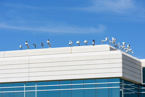 Multiple and different types outdoor security cameras cover multiple angles from the rooftop of modern office building under blue sky
