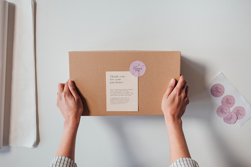 Hands of an unrecognisable online store owner holding a package with a thank you note before sending it to a customer