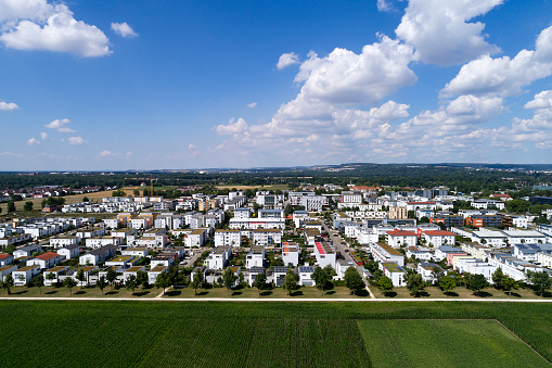 Aerial view of a new residential district with modern houses and apartment buildings in summer landscape and green fields under blue sky with beautiful clouds.