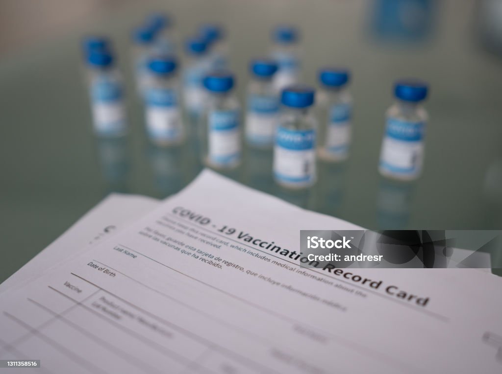 COVID-19 vaccine ampoules next to a vaccination record card Close-up on COVID-19 vaccine ampoules next to a vaccination record card â immunization concepts. **DESIGN ON DOCUMENT WAS MADE FROM SCRATCH BY US** Vaccination Stock Photo