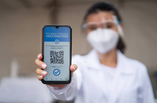 Healthcare worker holding a COVID-19 immunity passport on her cell phone Close-up on a healthcare worker holding a COVID-19 immunity passport on her cell phone certifying her vaccination status. **DESIGN ON SMARTPHONE WAS MADE FROM SCRATCH BY US** vaccine passport photos stock pictures, royalty-free photos & images