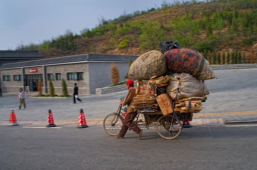 Beijing,China - April,30,2009: A Chinese man struggles with his load of recycle material as his three wheel bicycle pulls him downhill. This is at the entrance to the Great Wall of China in Beijing.