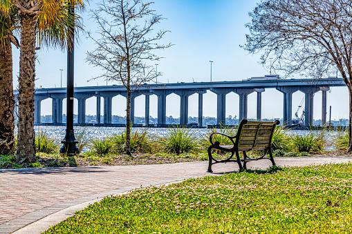 A park bench along the sidewalk of a landscaped public park along the Jacksonville Riverwalk.
