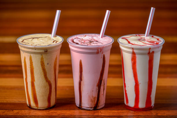 Milk shakes in plastic cups and straws on a dark wooden table. stock photo