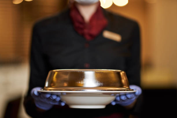 Selective focus photo of covered plate in hands of waitress Cropped photo of lady in uniform wearing rubber gloves and holding a plate with lid on room service stock pictures, royalty-free photos & images