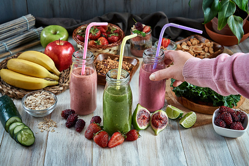 Young woman hands taking smoothie from wooden table. Healthy eating.