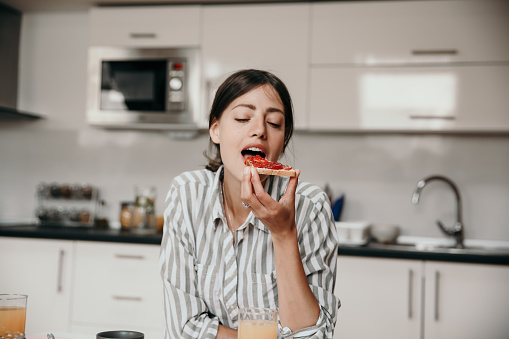 Portrait of a beautiful young woman having her toast with jam, wearing a striped shirt, ready  to enjoy the bite. Breakfast concept