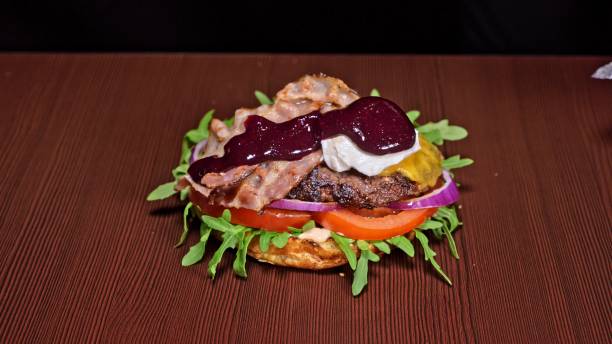 istock Craft burger is cooking on black background. Consist: sauce, arugula, tomato, onion, bacon, currant sauce, ricotta cheese, air bun and marble meat. 1311385196