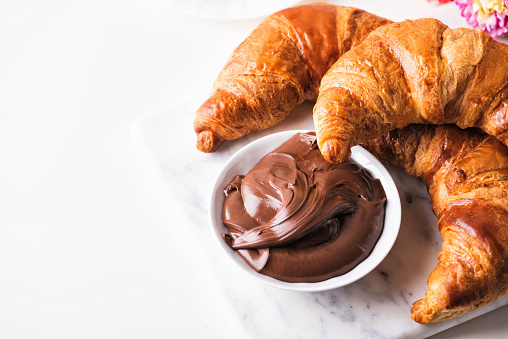 Croissant with chocolate hazelnut spread on a white table. Continental breakfast with flowers
