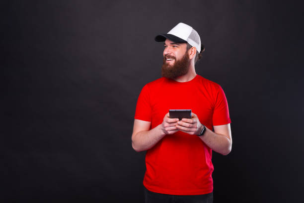 photo of bearded hipster man in red t-shirt holding tablet and looking away over black background - hipster people surfing the net internet imagens e fotografias de stock