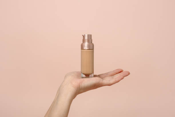 istock Hand holding makeup liquid found, Applying foundation for makeup. Woman's hands with neutral manicure holding bottle of concealer or toner foundation, copy space, banner, flyer 1311402356