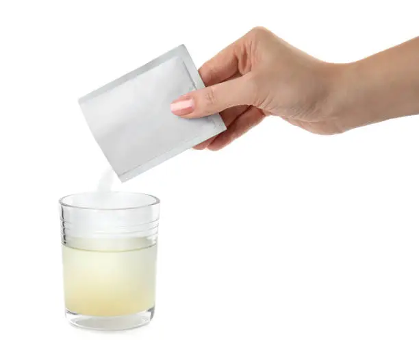 Woman pouring powder from medicine sachet into glass of water on white background, closeup