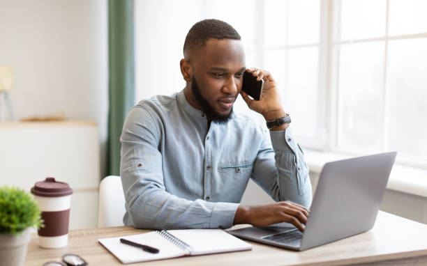 istock Serious African Business Guy Talking On Phone At Workplace Indoor 1311404996