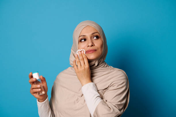 Beautiful Muslim woman with covered head in hijab applying micellar lotion and removing make up from her lips