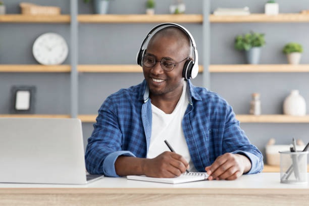 istock E-education. Happy black mature man using laptop and taking notes, listening online course 1311407953