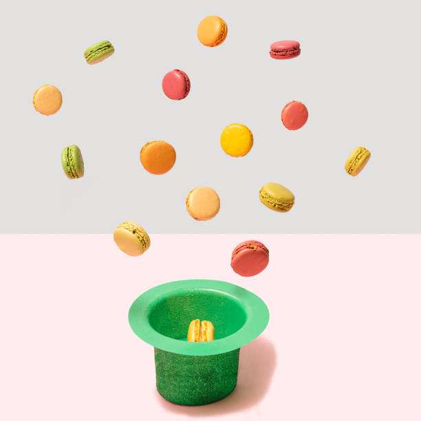 Unique levitate arrangement of delightful, colorful macarons and green hat. A concept made with ultimate gray and pastel pink background. Gravity concept.