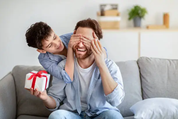 Photo of Happy father's day. Son congratulating his daddy, covering his eyes from behind and giving present at home