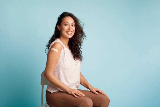 istock Young Woman Showing Vaccinated Arm After Injection On Blue Background 1311408934