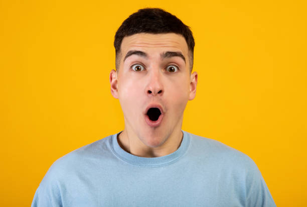istock Funky young guy opening mouth in shock, shouting WOW or OMG at camera on orange studio background 1311409078