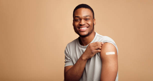 Portrait Of Vaccinated African Man Showing His Arm, Beige Background Covid-19 Vaccination. Portrait Of Happy Vaccinated African Man Showing His Arm After Coronavirus Antiviral Vaccine Shot Over Beige Background. Covid Immunization Campaign Concept. Panorama arm stock pictures, royalty-free photos & images