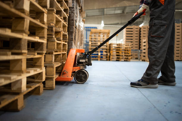 istock Working at warehouse. Low angle view of unrecognizable worker lifting palette with manual forklift. 1311409623