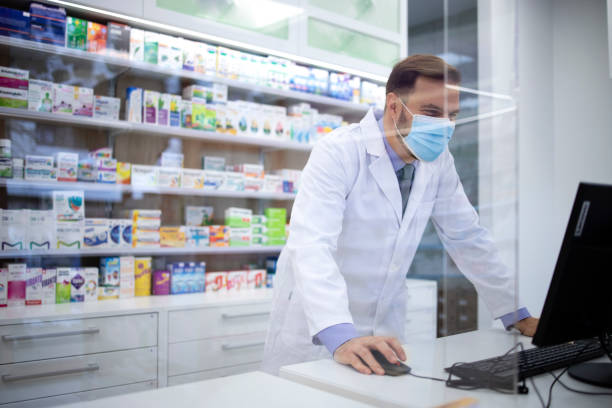 Pharmacist wearing face protection mask and white coat selling vitamins in pharmacy store during corona virus pandemic. Pharmacist wearing face protection mask and white coat selling vitamins in pharmacy store during corona virus pandemic. chemist stock pictures, royalty-free photos & images