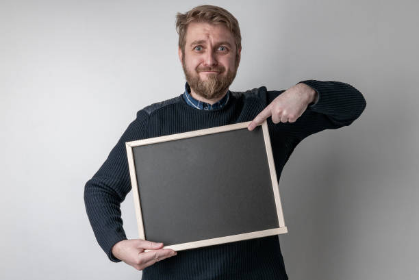 istock man with beard pointing on blank blackboard scared in shock with a surprise face, afraid and excited with fear expression 1311413720