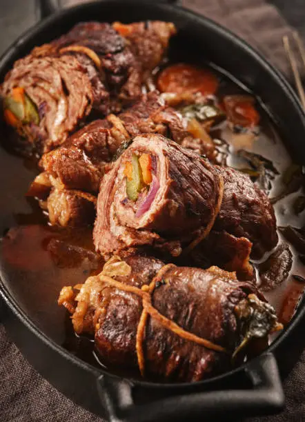 Dish of beef, bacon and pickle roulades in gravy seasoned with vegetables for a traditional regional German dinner. German traditional cuisine beef roulade with bacon and vegetables.