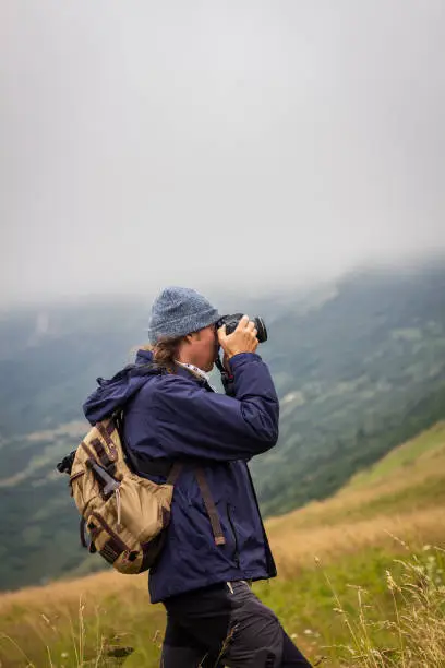 Photo of Man with backpack is photographing during hike in mountains
