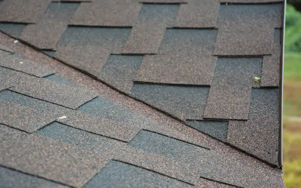 A close-up on the problem, critical area of a roof valley and drip edge covered with asphalt dimensional shingles above metal roof flashing.