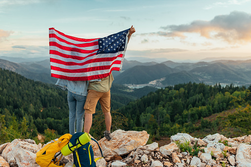 Couple standing on the top of a mountain and holding the American flag