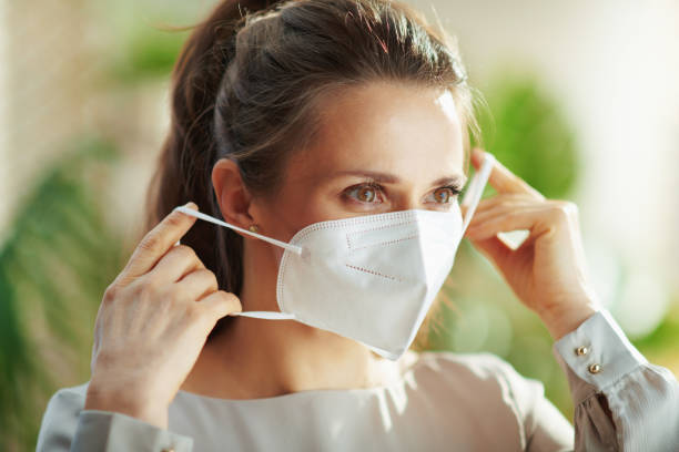 woman in grey blouse wearing ffp2 mask covid-19 pandemic. middle aged woman in grey blouse wearing ffp2 mask. person wearing n95 mask stock pictures, royalty-free photos & images