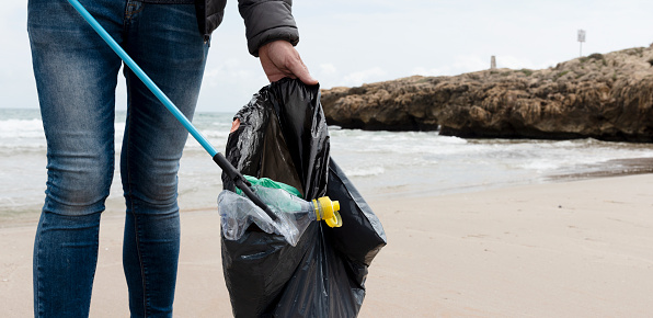 a man is collecting some waste, such as cans, bottles or bags, from the sand of a lonely beach, as an action to clean up the natural environment