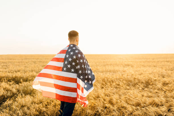 istock Young man holding American flag while standing on wheat field 1311422882