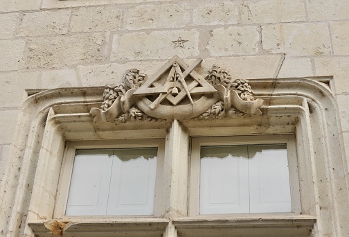 Pediment of a window with freemason symbols of France carved in tuf stone located in the old city of chinon in france
