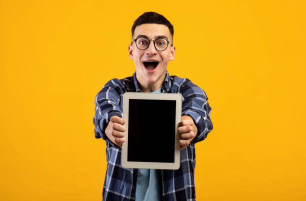 istock Overjoyed millennial man showing tablet computer with mockup for website or app design on orange background 1311425487